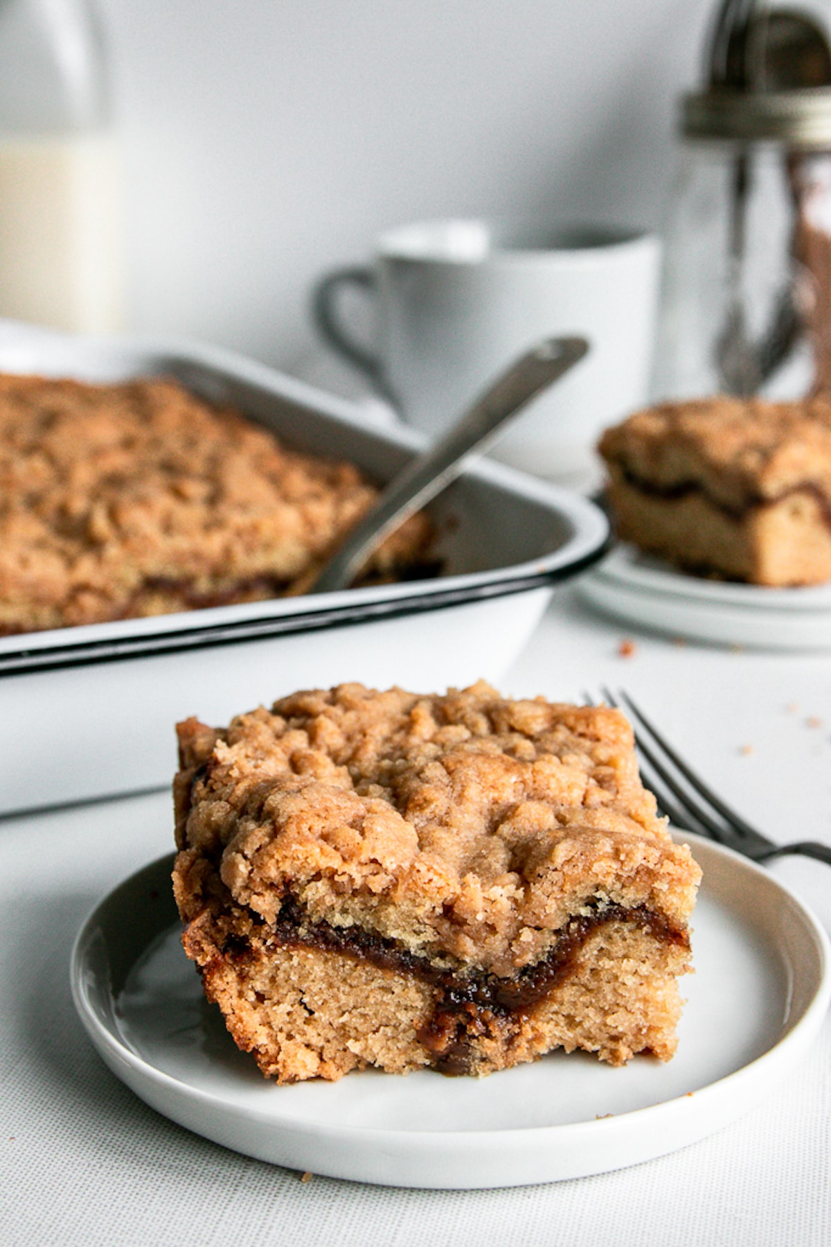 Coffee cake in an enamel baking pan with a slice cut out on a plate.