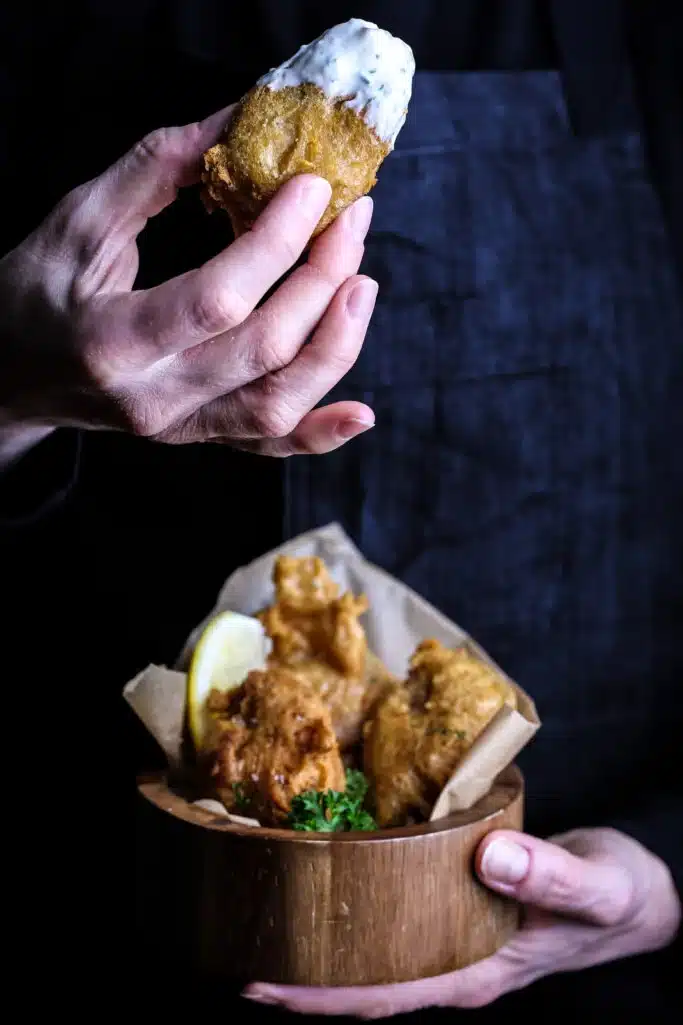 Deep fried jackfruit in a wooden bowl with a man picking up a piece dipped in sauce.