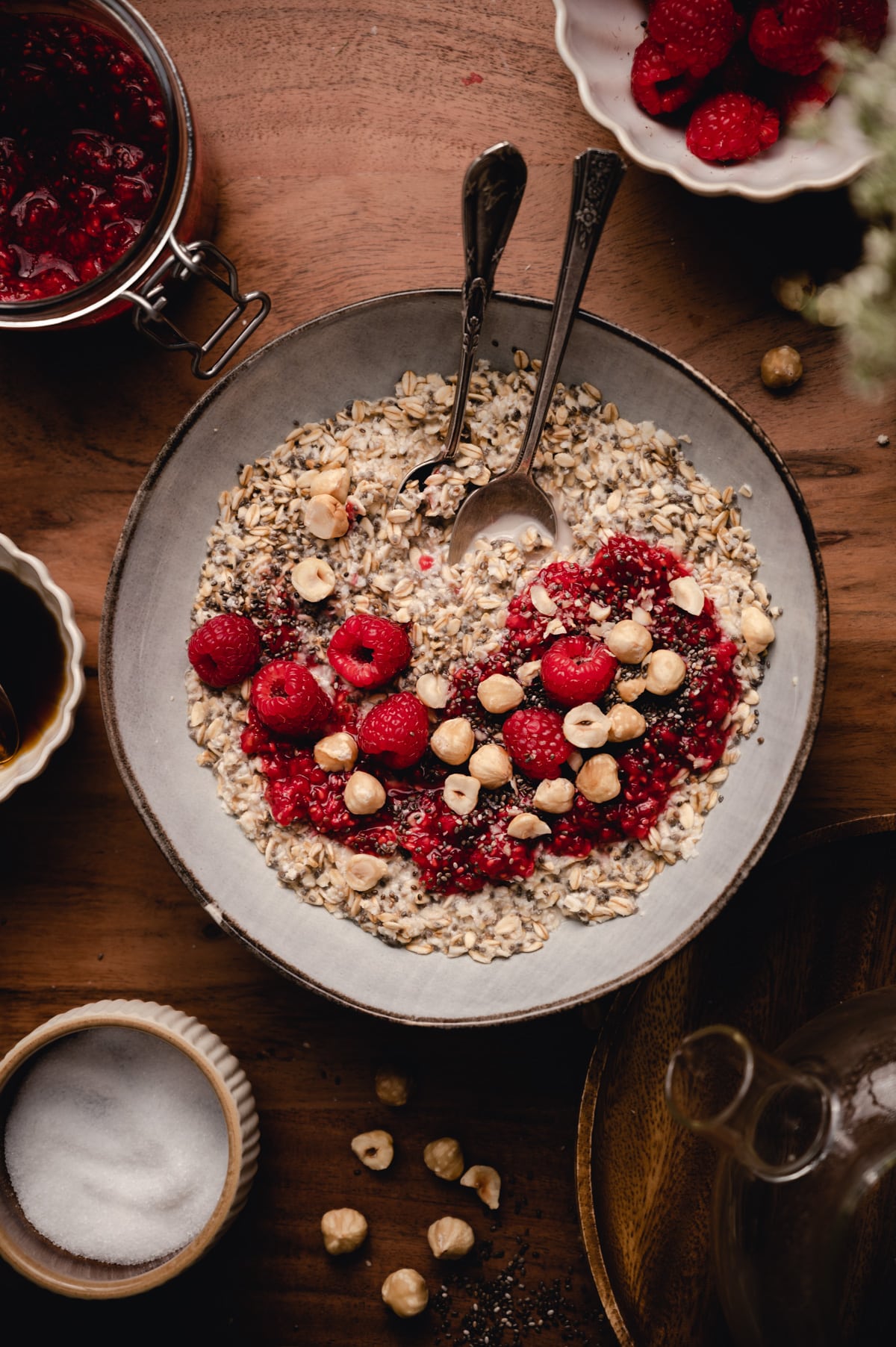 Top down photo of chia oats with fresh raspberries hazel nuts on top surrounded by ingredients.