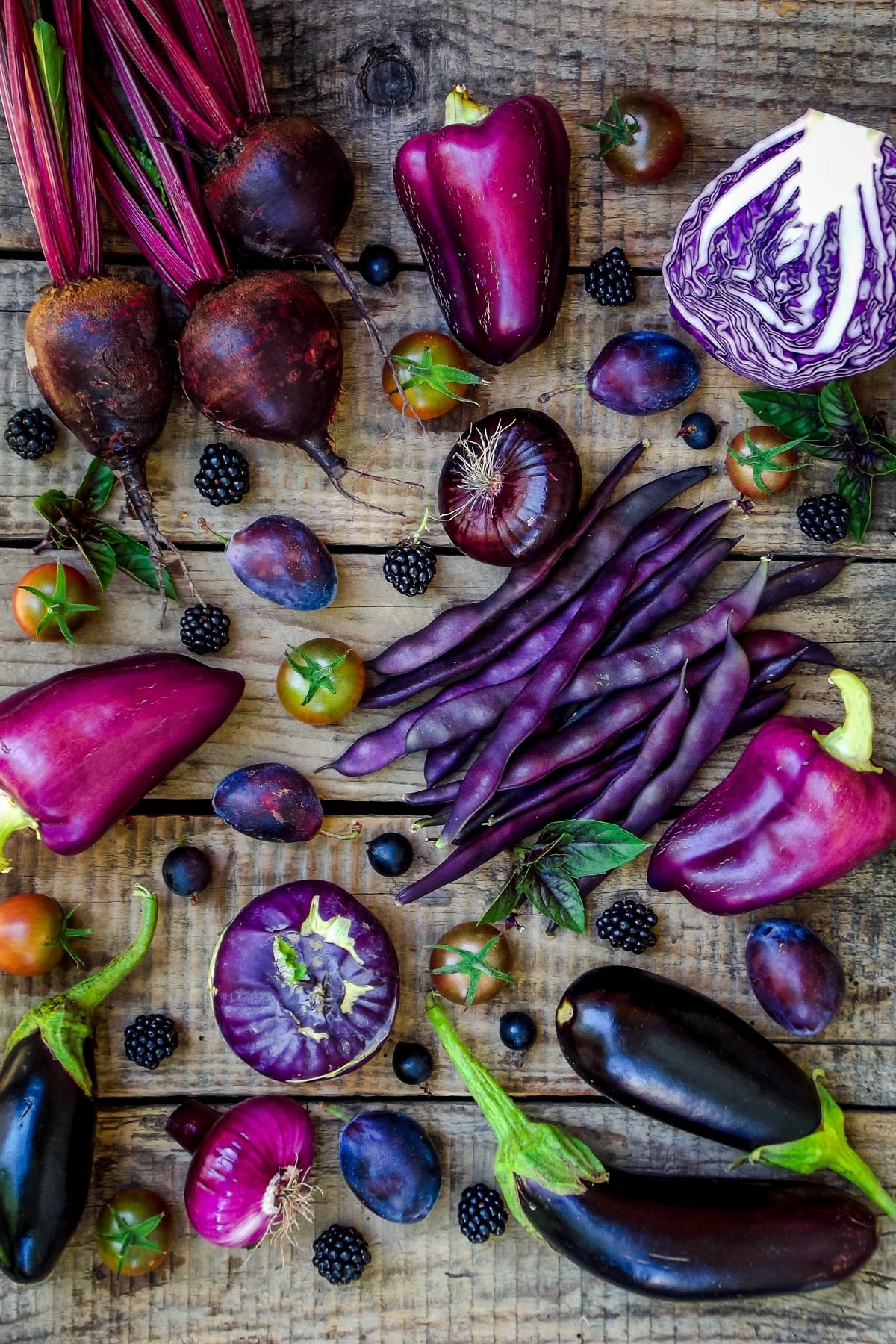 Rustic wooden table covered in purple fruits and vegetables.