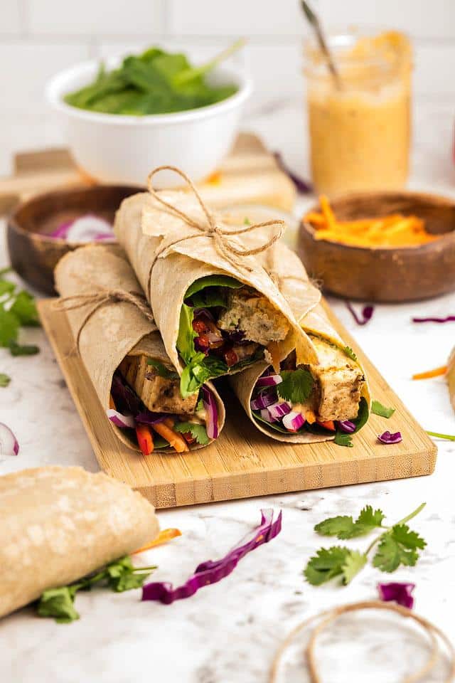 Four vegan tofu wraps on a wooden cutting board.