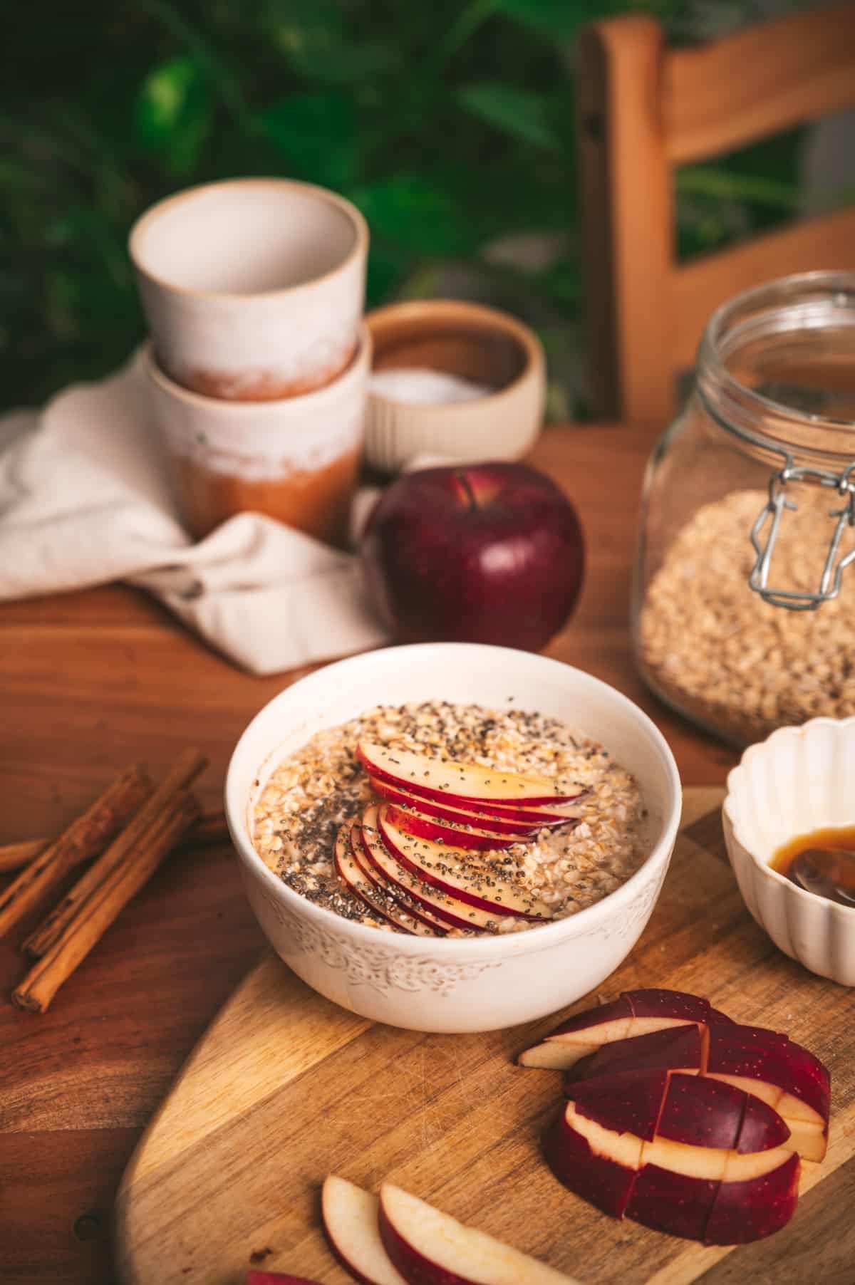 Table set with cups, ingredients, and a bowl of apple cinnamon oatmeal topped with sliced apples.