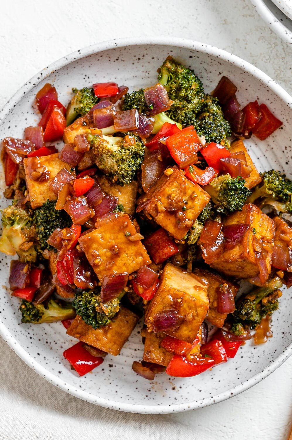 Vegan tofu and broccoli served in a white bowl with chopsticks.