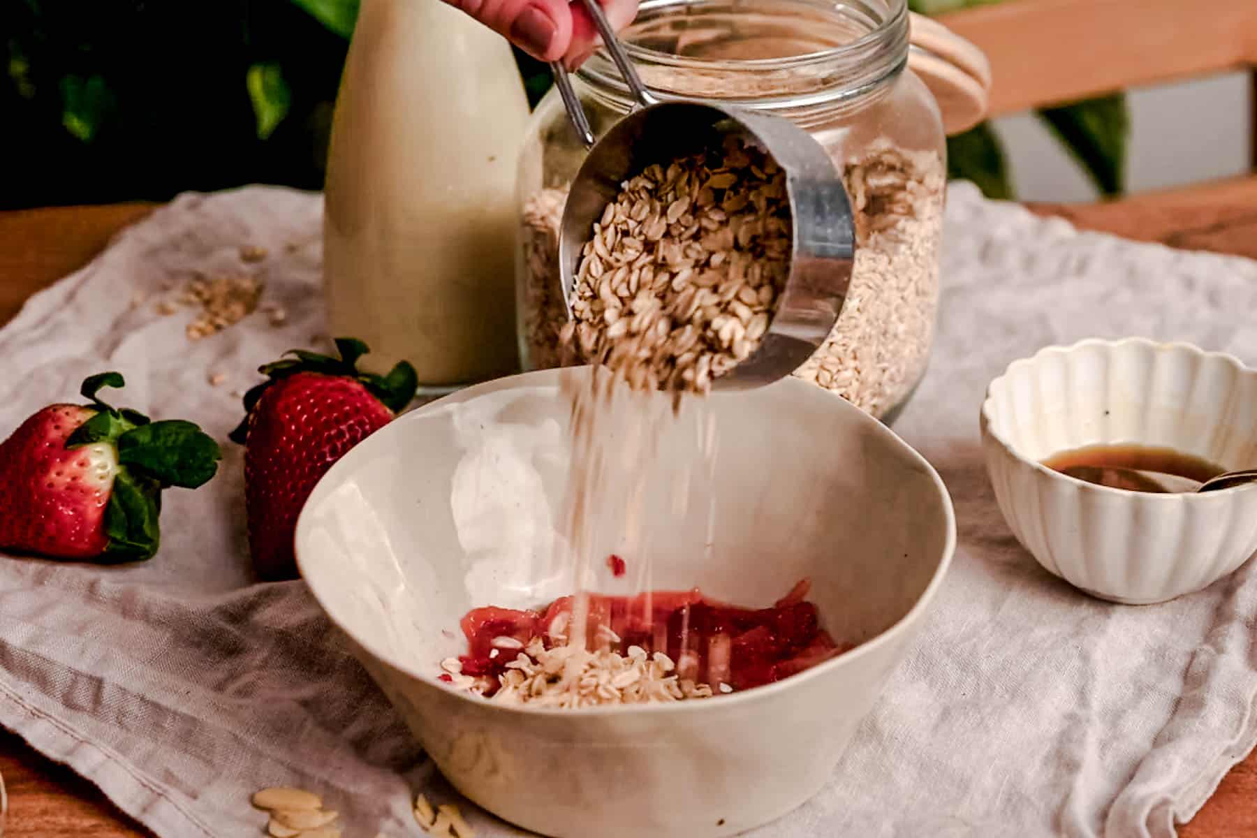 Pouring oats into a bowl with mashed strawberries.