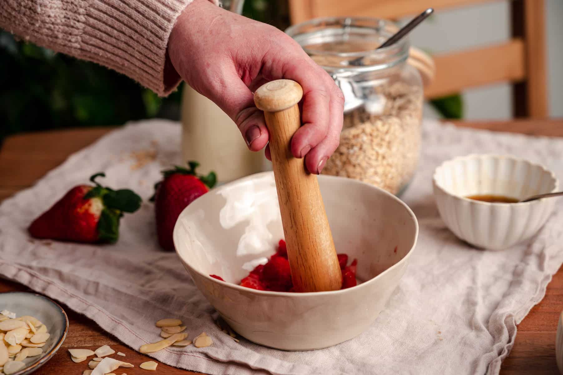 Muddling fresh strawberries in a bowl.