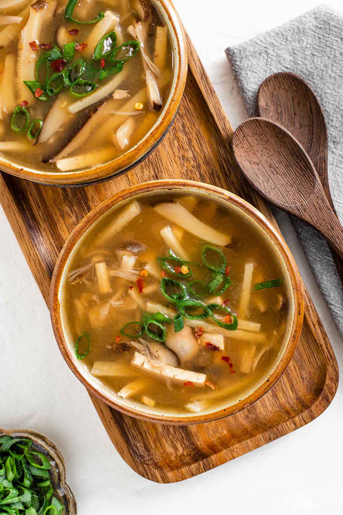 A vegan jackfruit soup in two bowls on a wooden tray.