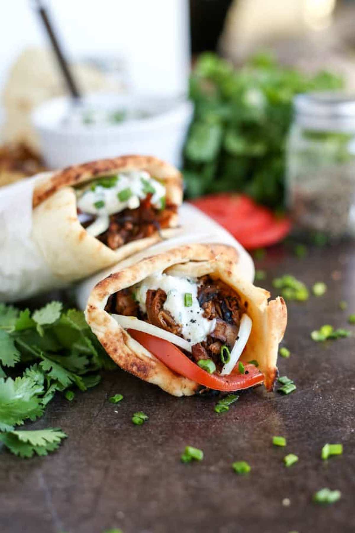 Two gyros resting on top of each other wrapped in white paper.