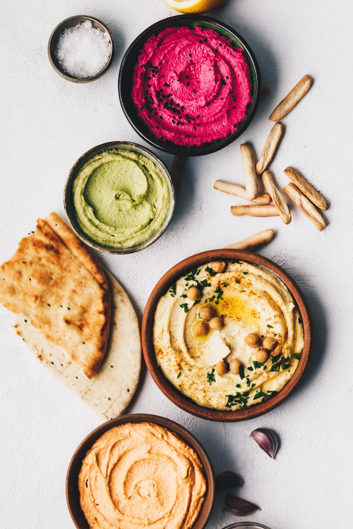 Garbanzo bean hummus, herbs hummus, beetroot hummus and lentils humus with bread sticks, pita bread, and finishing salt.