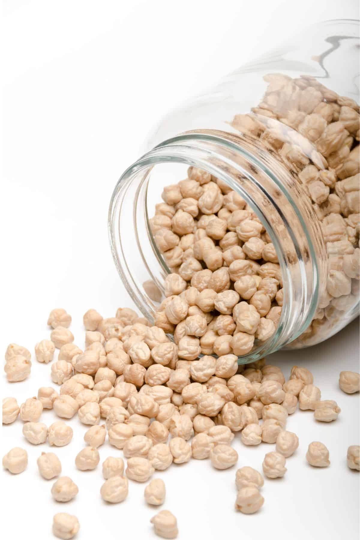 Glass jar tipped over with dried chickpeas spilling out.
