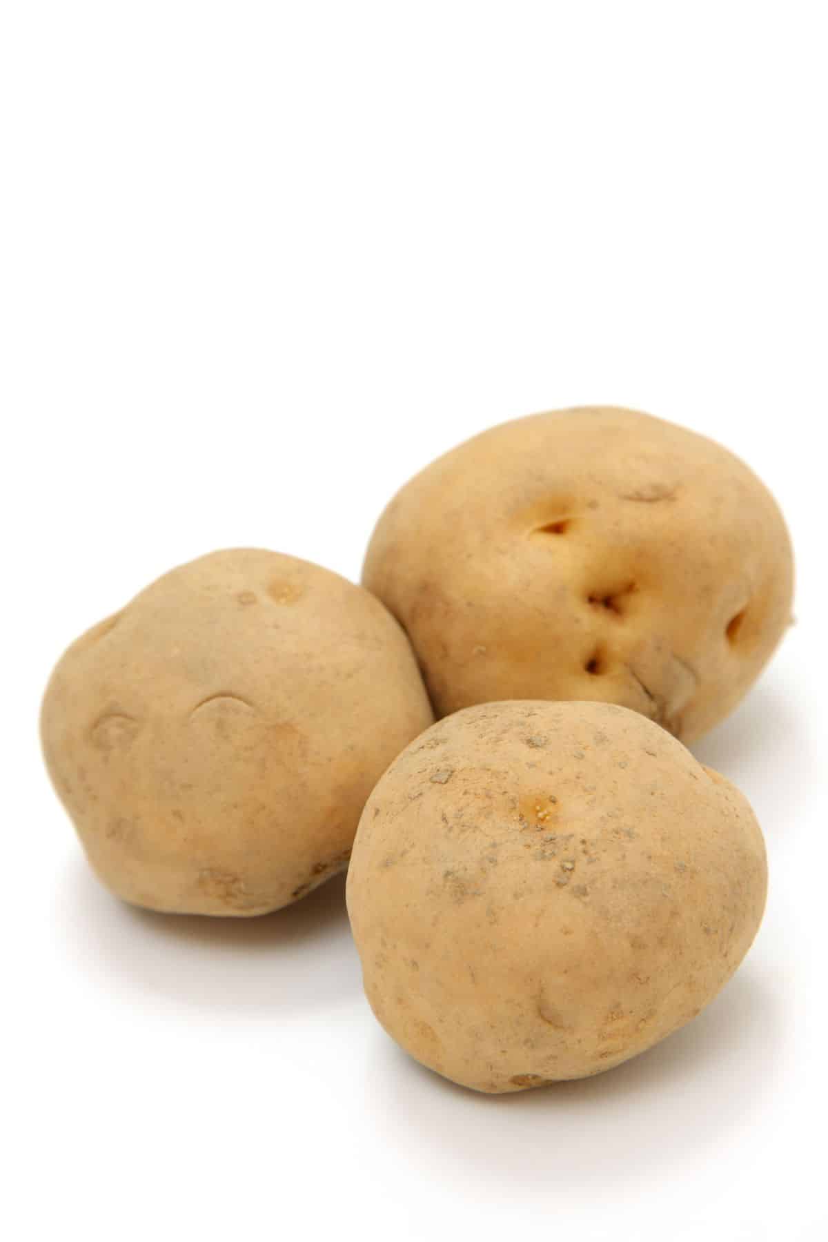 Tan skinned potato with white flesh on a white surface.