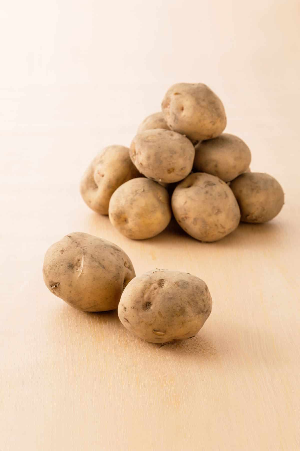 Tan skinned white flesh potatoes on a peach colored table top.