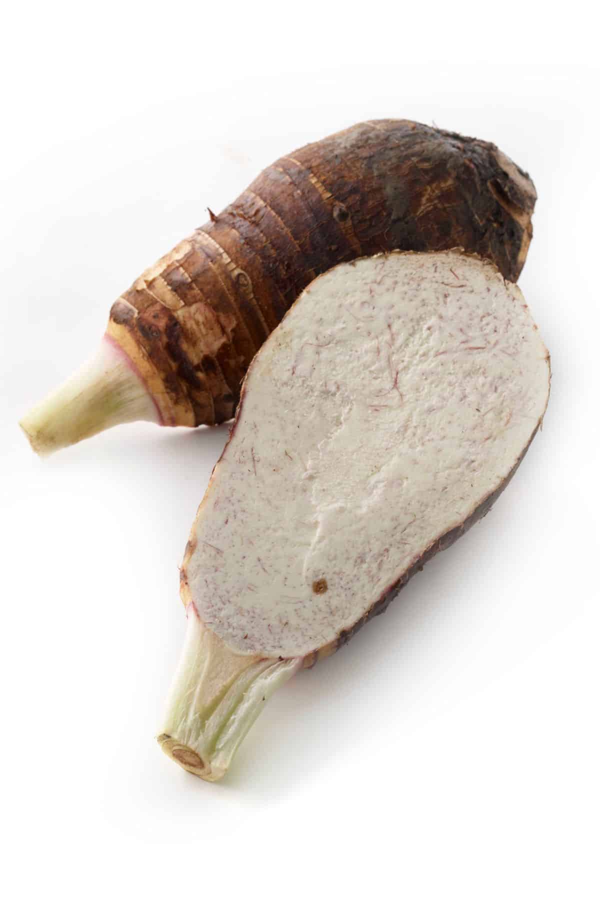 Two pieces of fresh taro with one cut in half showing the inside.