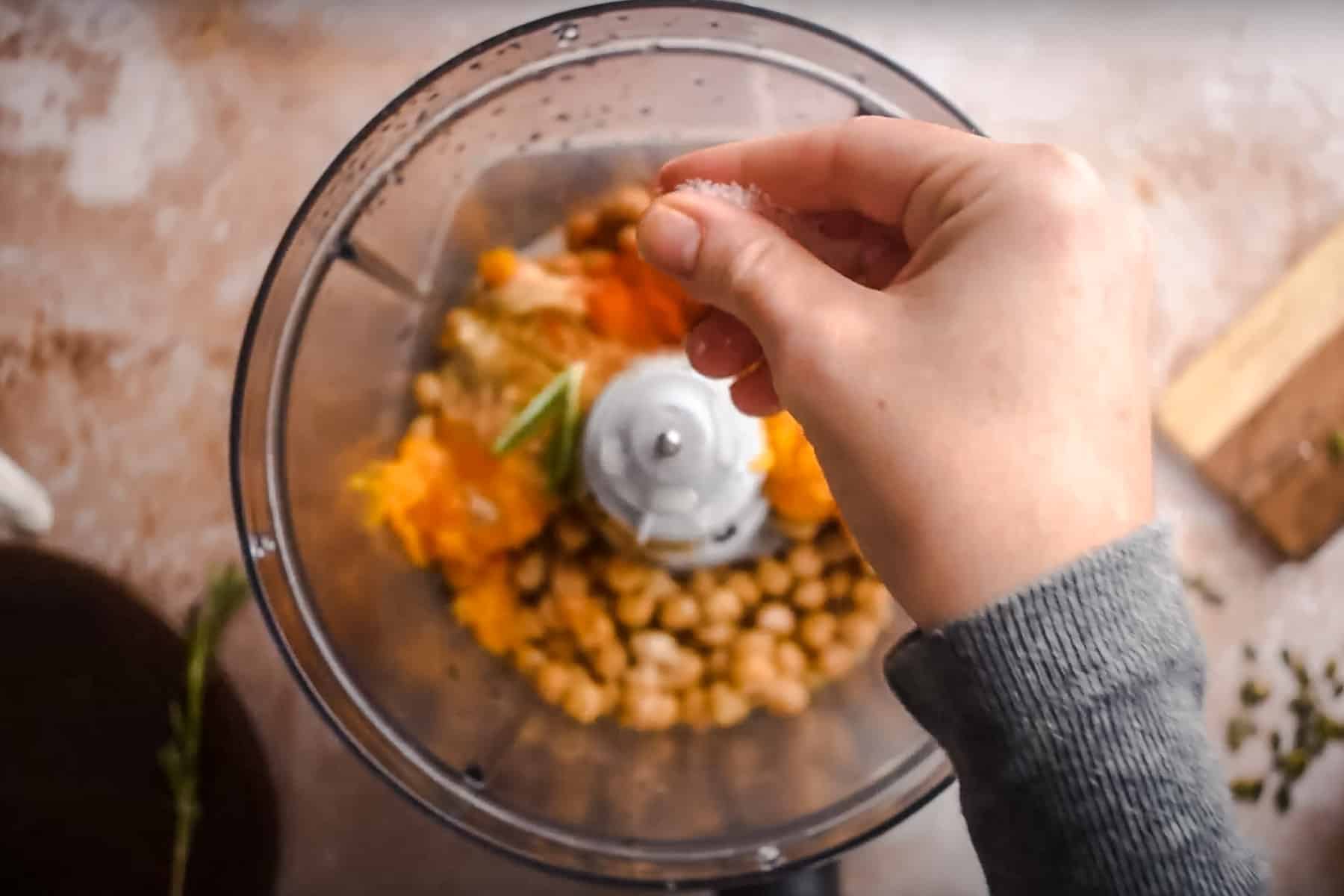 A person sprinkles salt into a food processor. 
