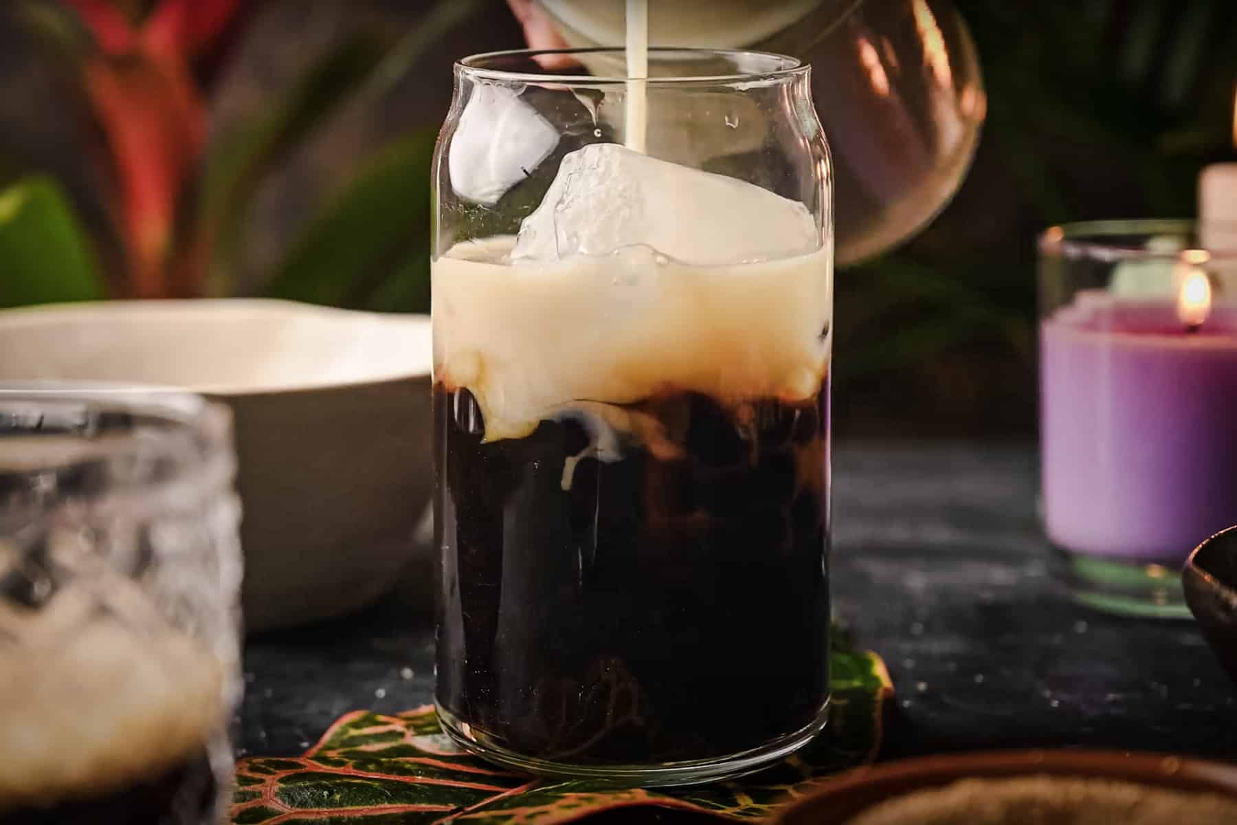 Milk is being poured into a glass of iced coffee.