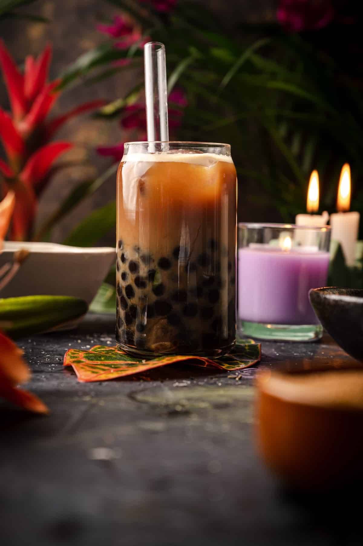 Freshly made coffee milk tea with tropical plant leaves around it.