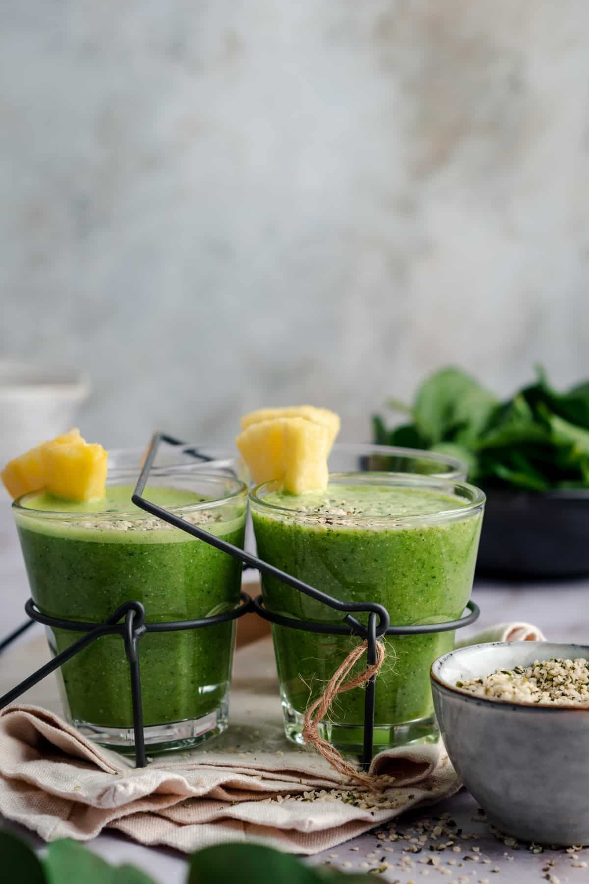 Green pineapple smoothie in clear glass cups with pineapple slices sticking out.
