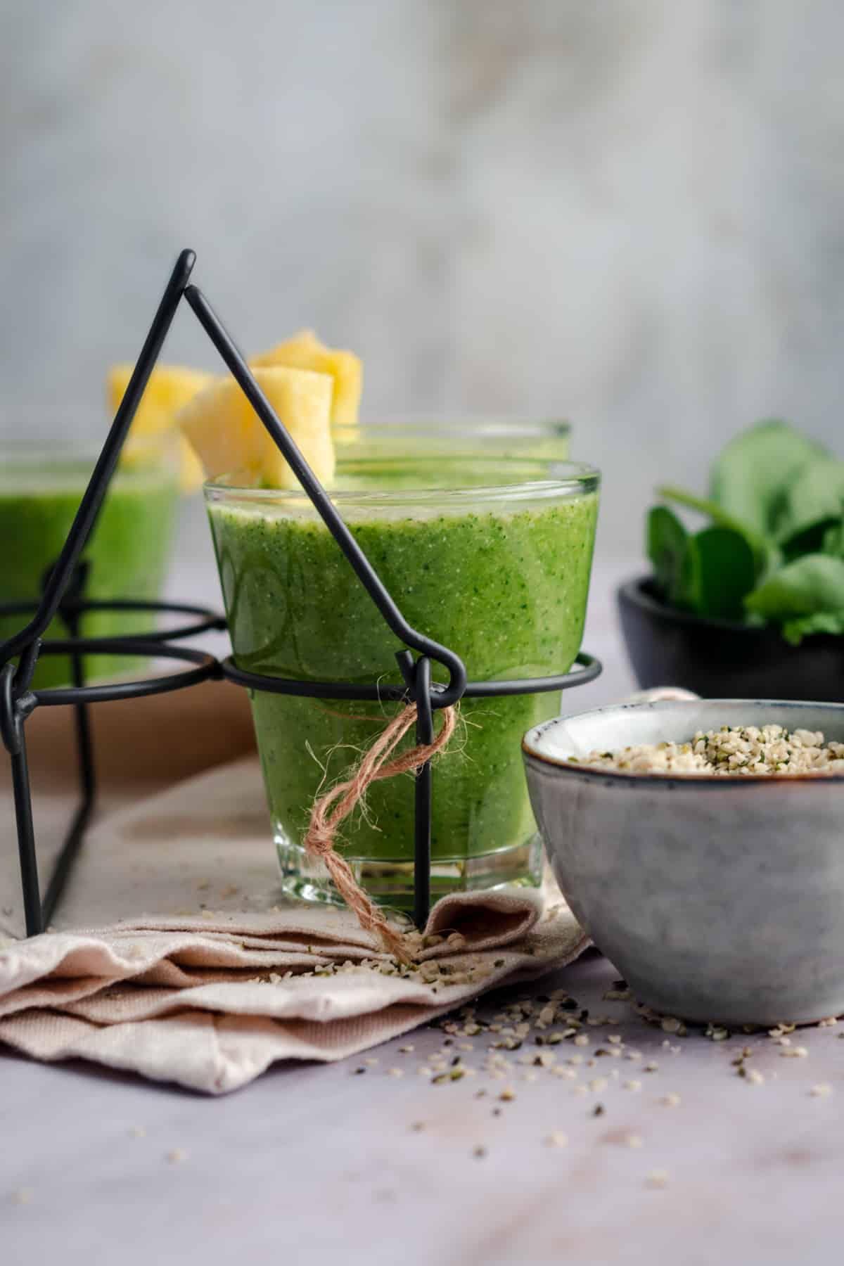 Black metal drink carrier with handle with three cups of green pineapple smoothie.