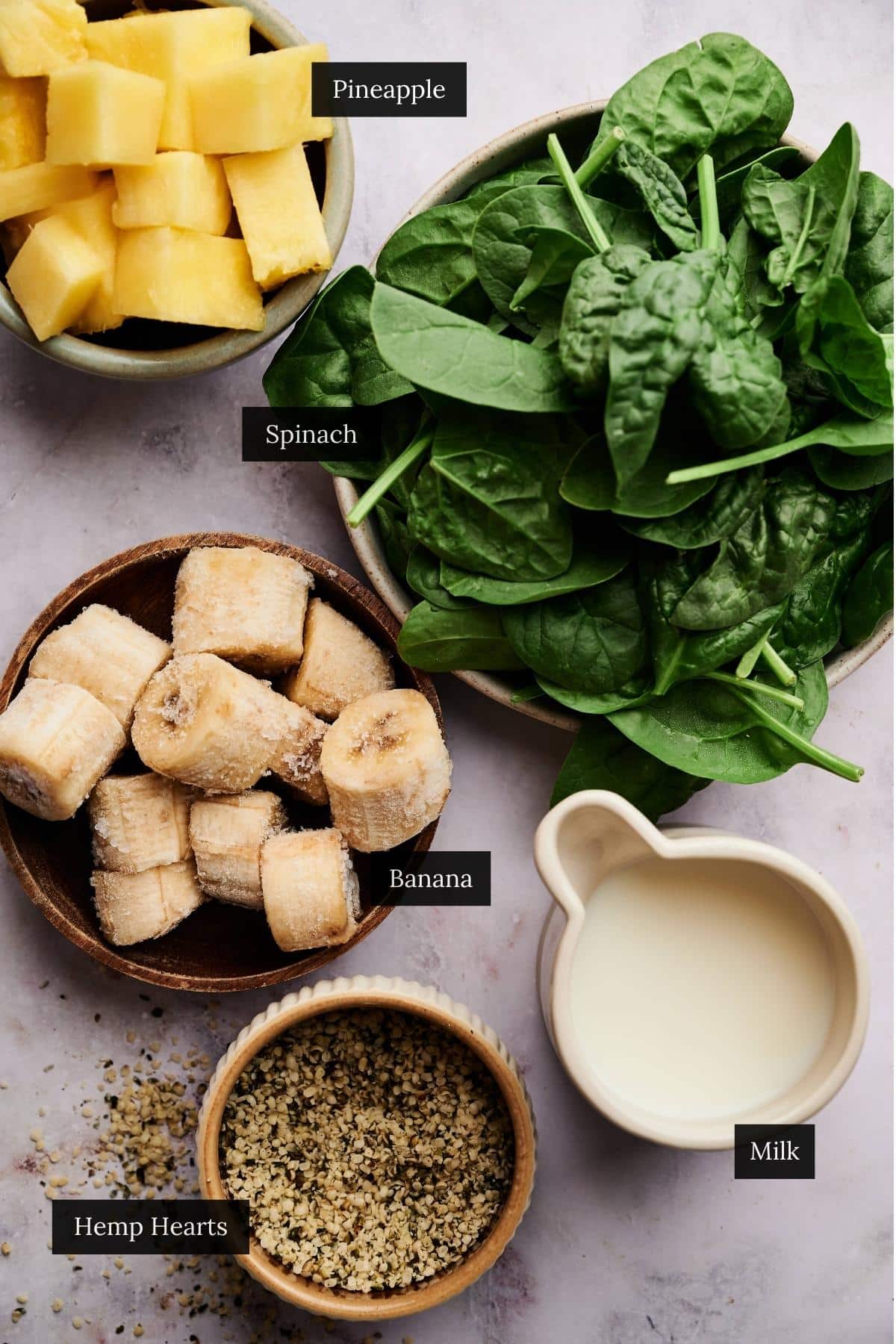 Ingredients for a homemade spinach pineapple smoothie on a marble counter with each ingredient labeled.