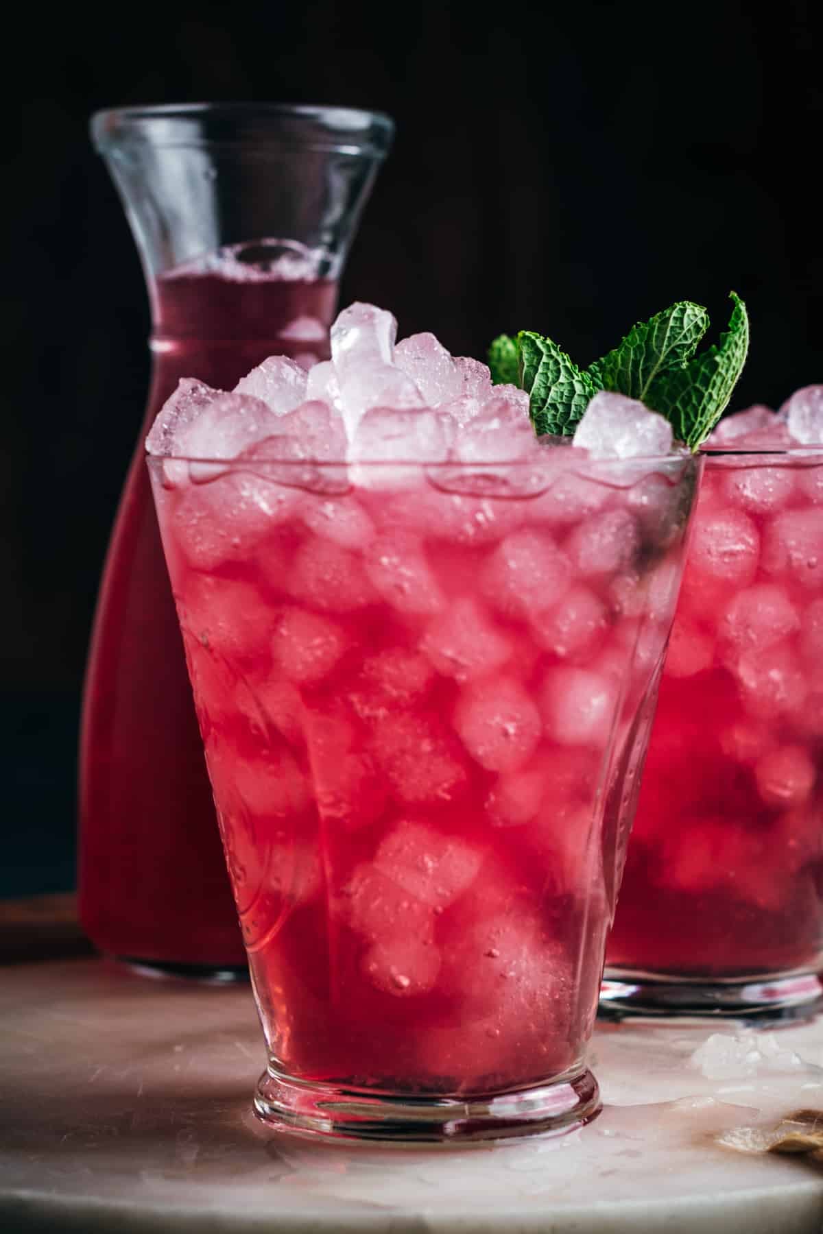 Two glasses with ice, pink lemonade, and mint leaves on a wooden table.