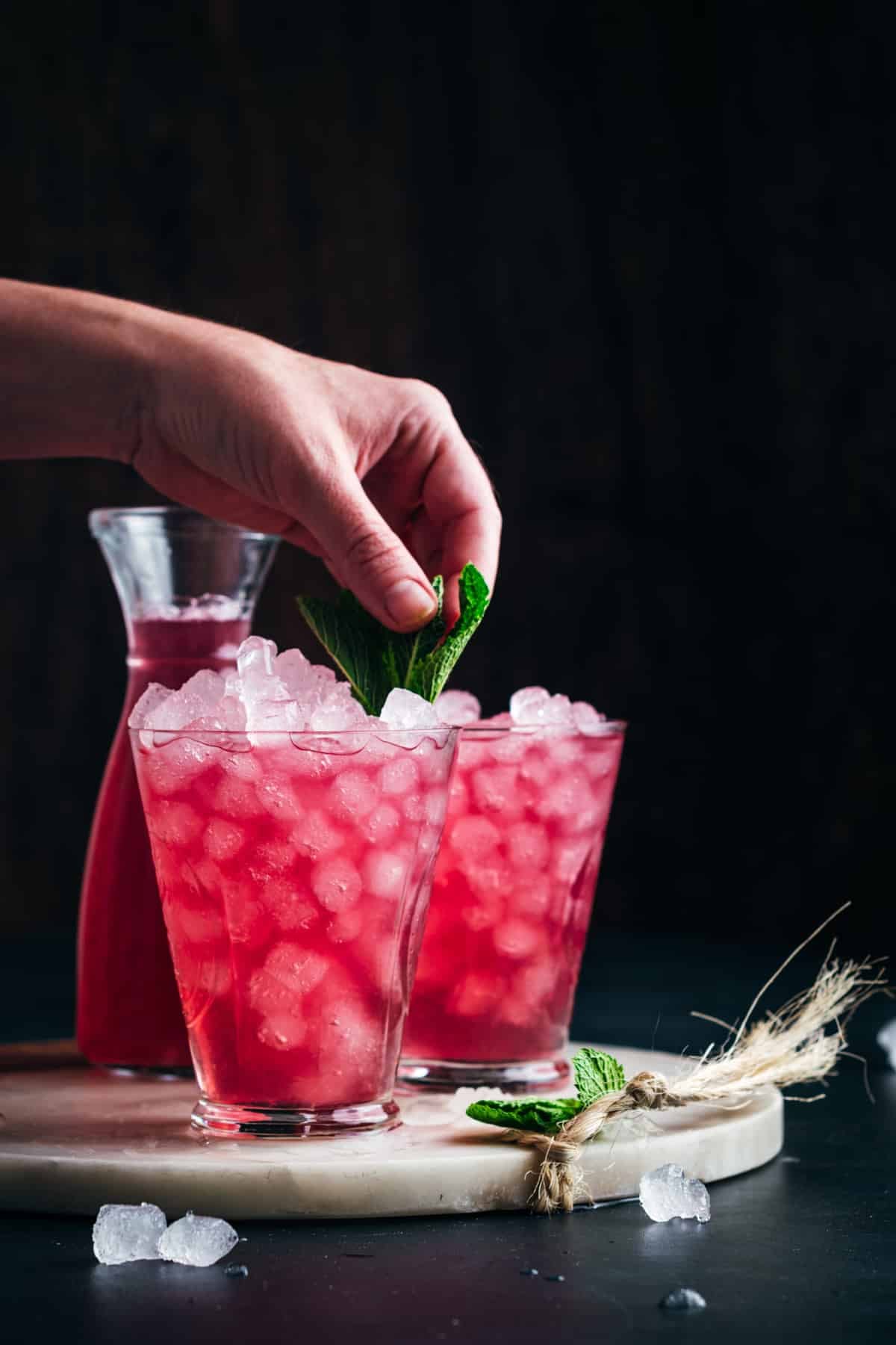 Woman placing mint leaves in a glass of cranberry lemonade.