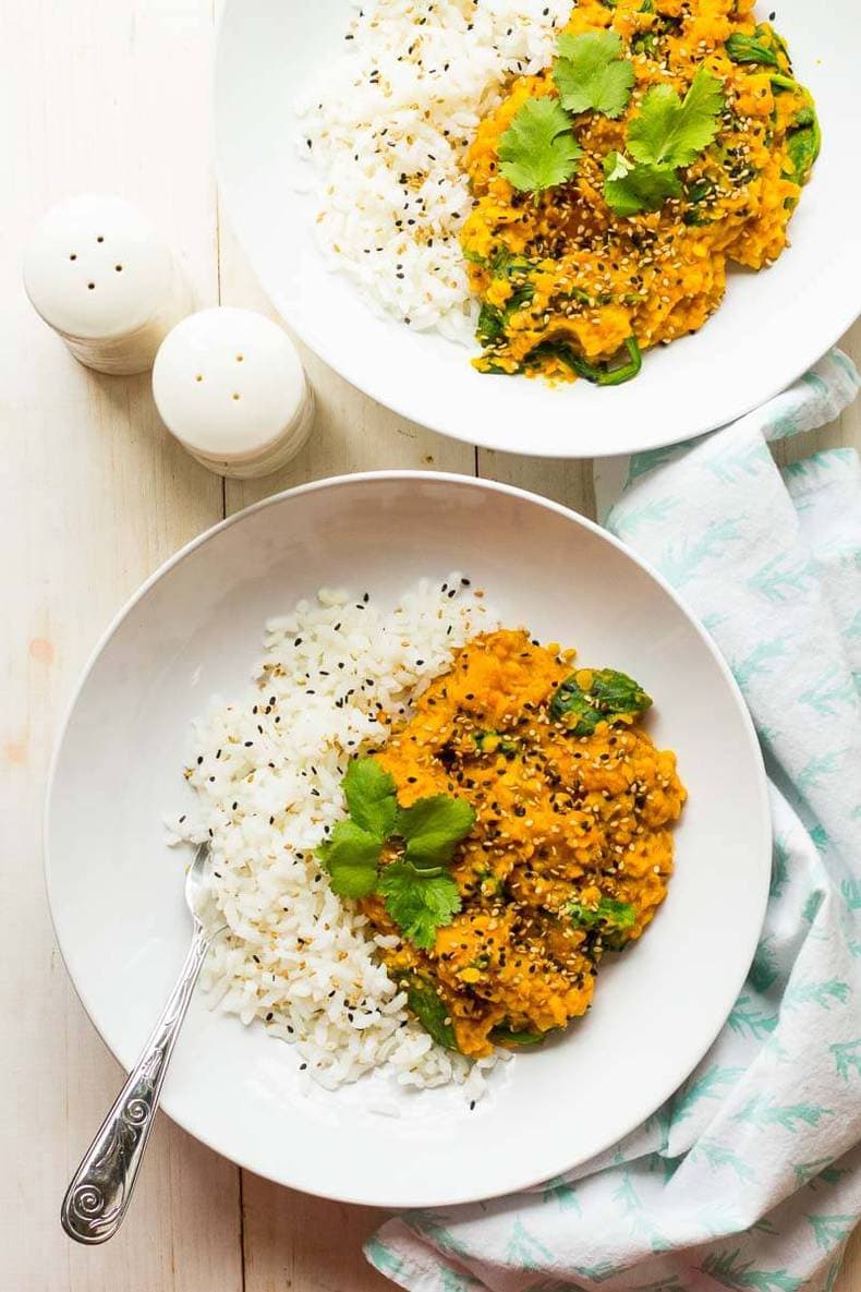 Two bowls of rice and curry on a wooden table.