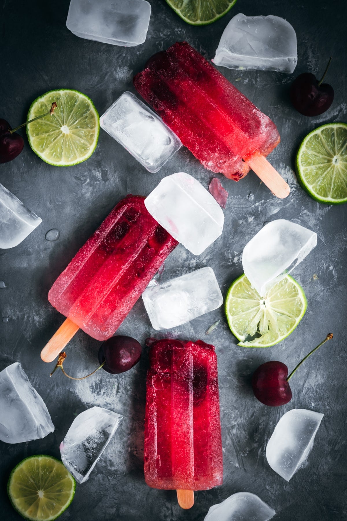 Cherry popsicles with ice cubes and lime slices.