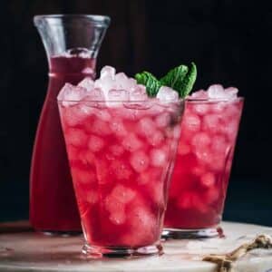 Two glasses of pink iced cranberry lemonade garnished with mint leaves.