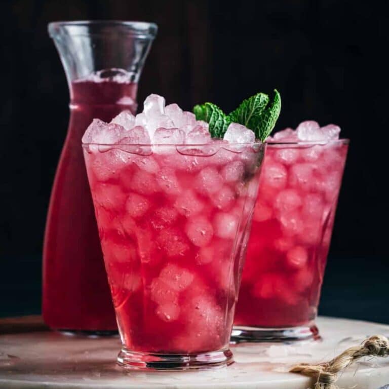 Two glasses of pink iced cranberry lemonade garnished with mint leaves.