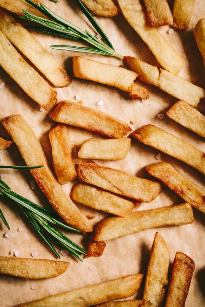 French fries on a baking sheet with rosemary sprigs.