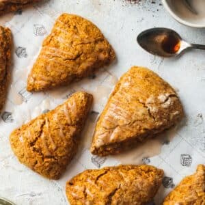 Five iced pumpkin scones are arranged on a patterned paper.