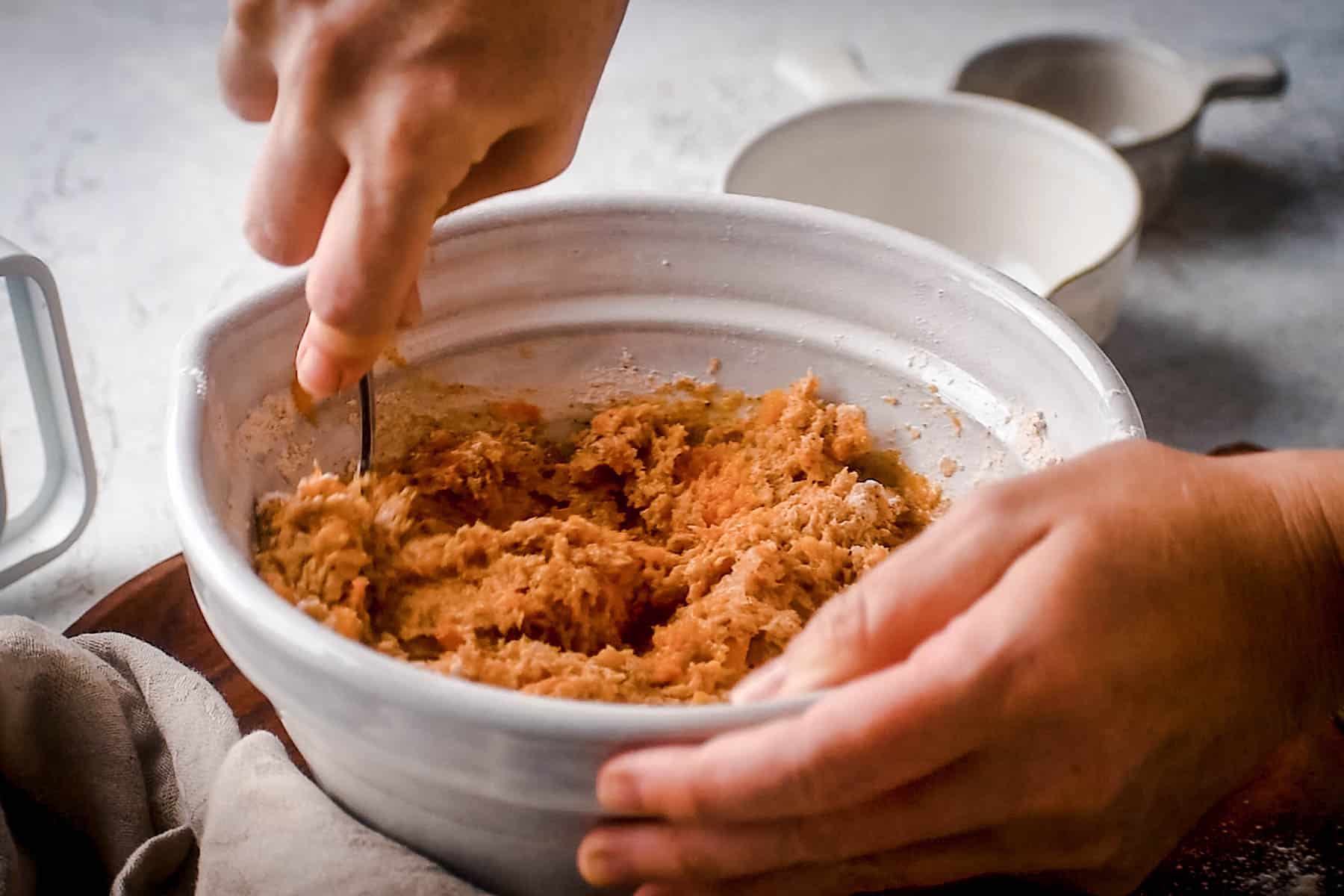 Person mixing dough in a white bowl with a spoon, preparing to make delicious pumpkin scones.