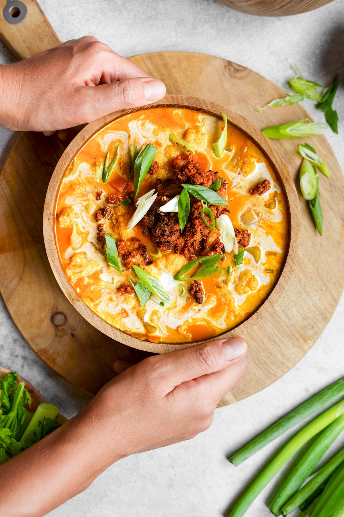 A person holding a bowl of soup on a wooden cutting board.