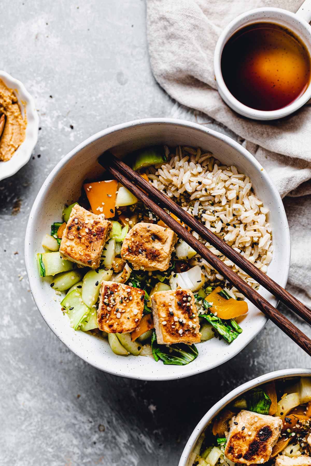 A bowl of tofu and vegetables with chopsticks.