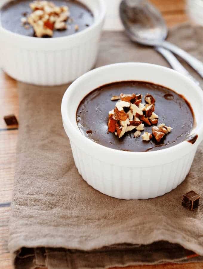 Two bowls of chocolate pudding with nuts on top.