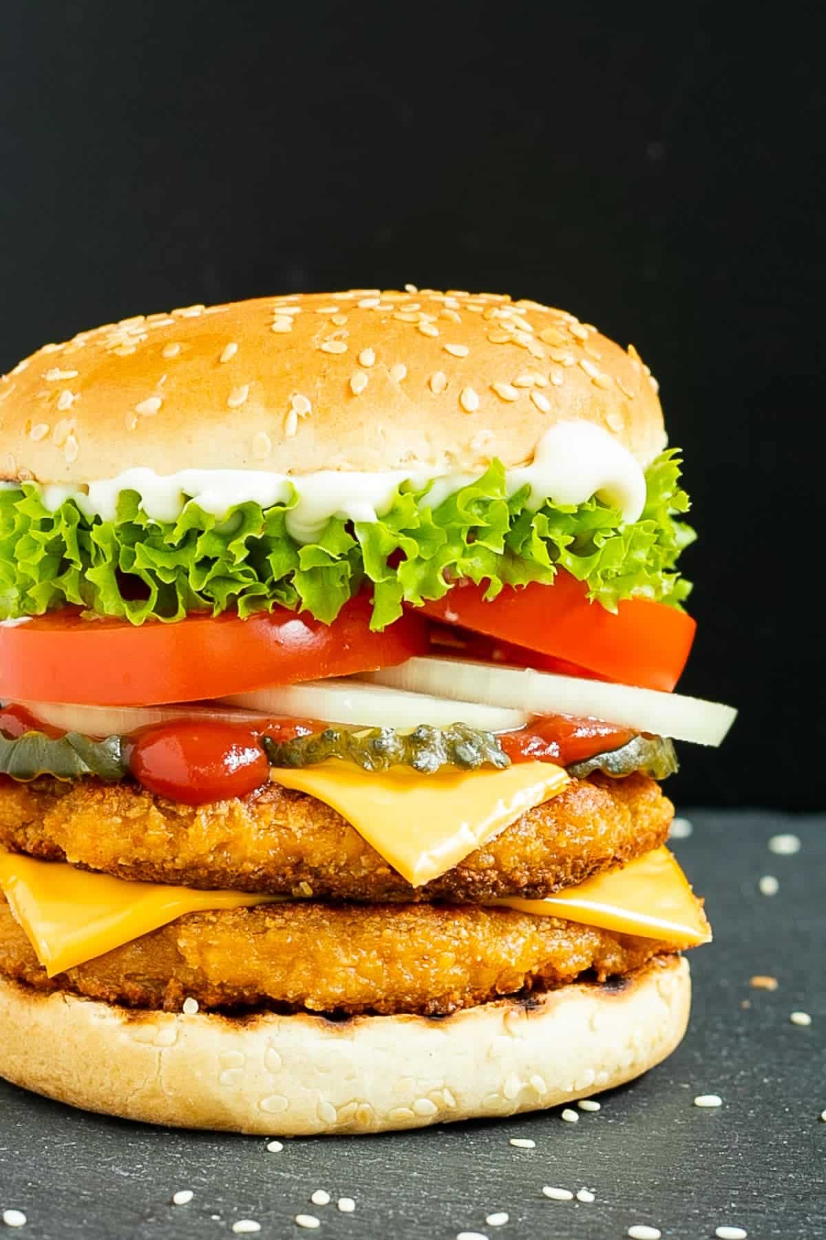 A burger with chicken, lettuce, tomatoes and cheese.