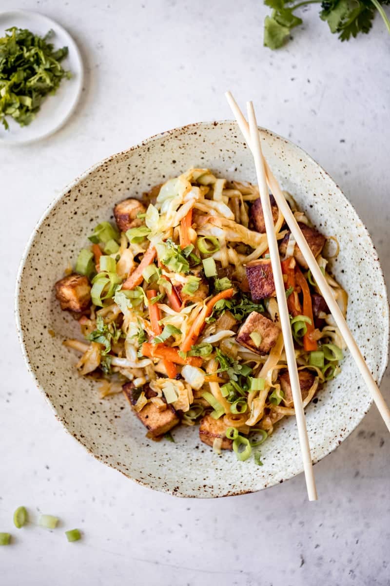 A bowl of noodles and vegetables with chopsticks.