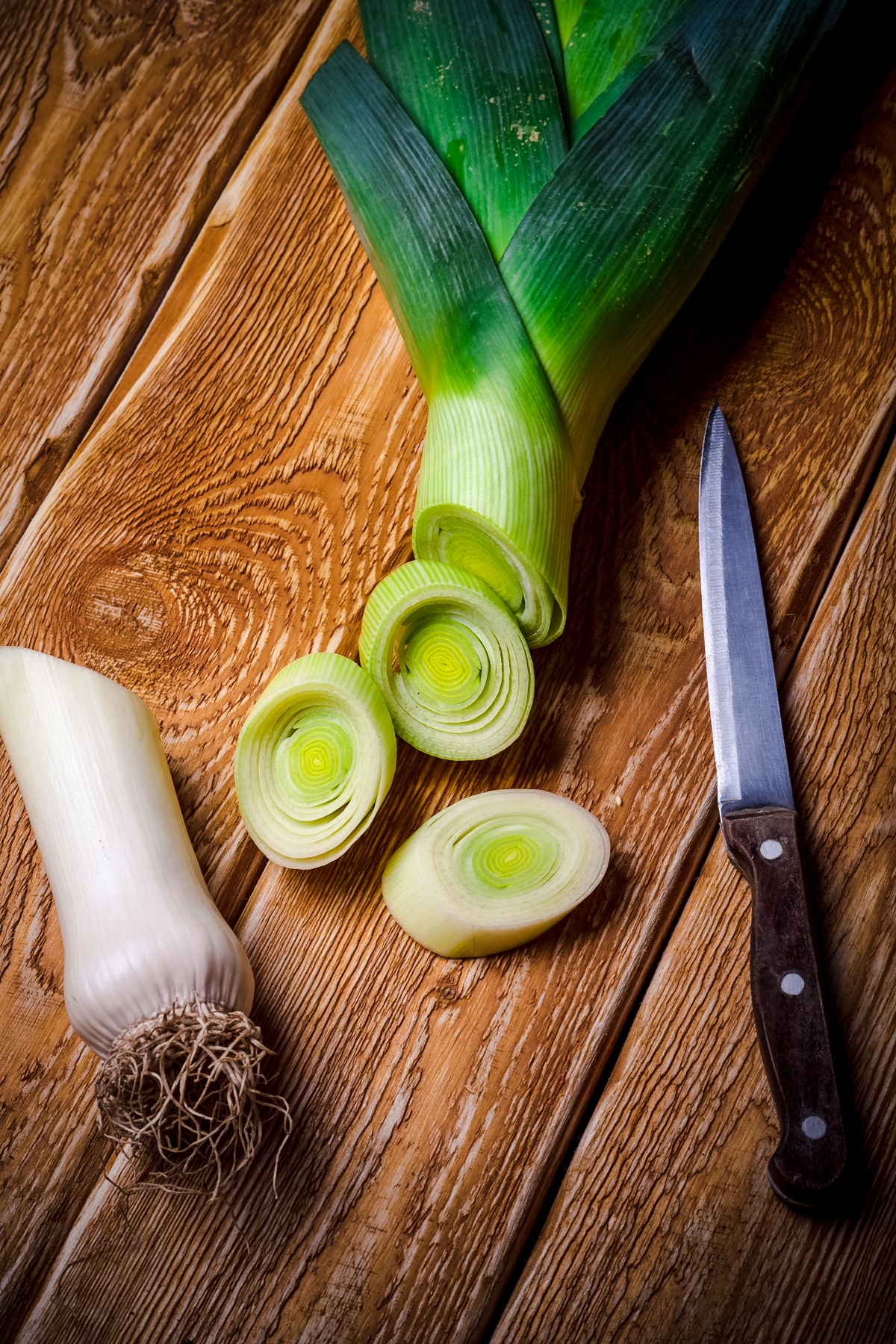 A leek and knife on a wooden table.