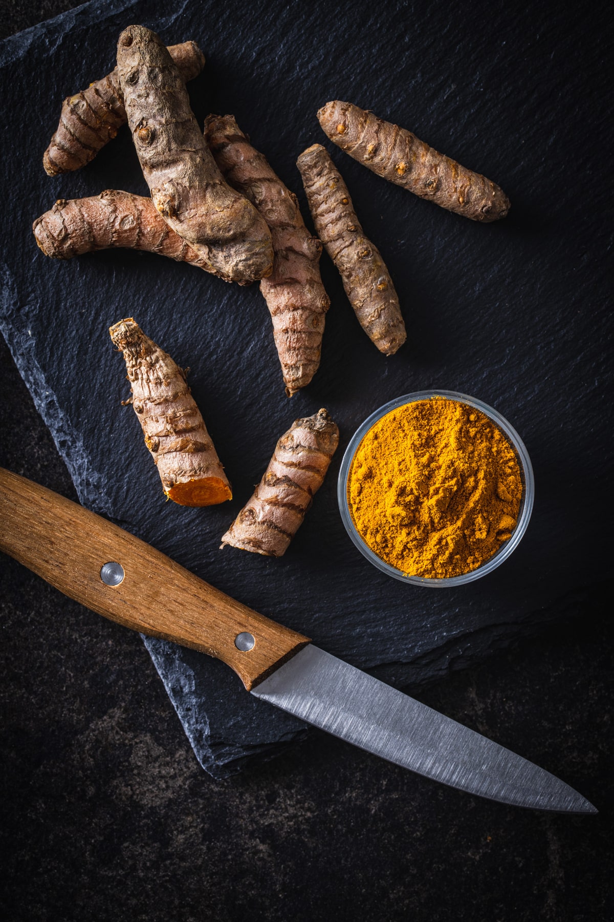 Tumeric powder and a knife on a black background.