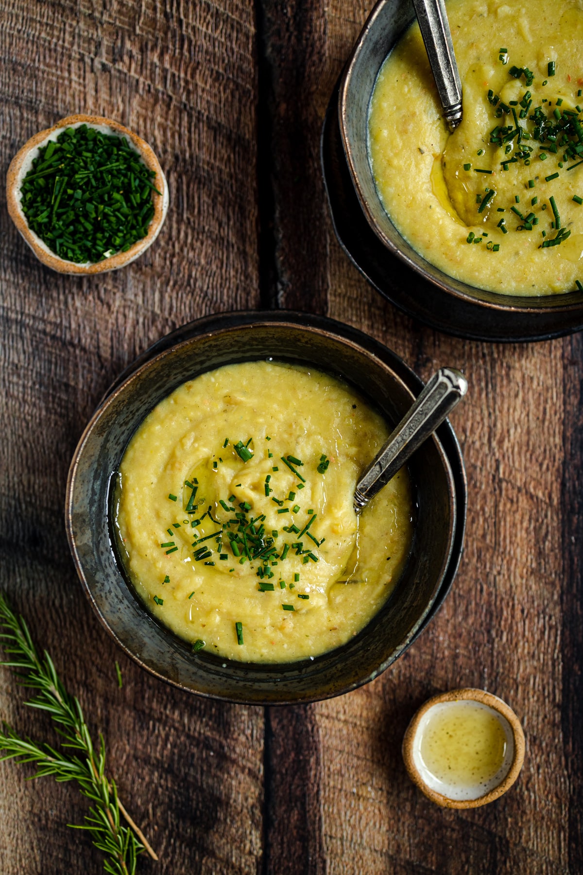 Two bowls of soup with herbs on a wooden table.