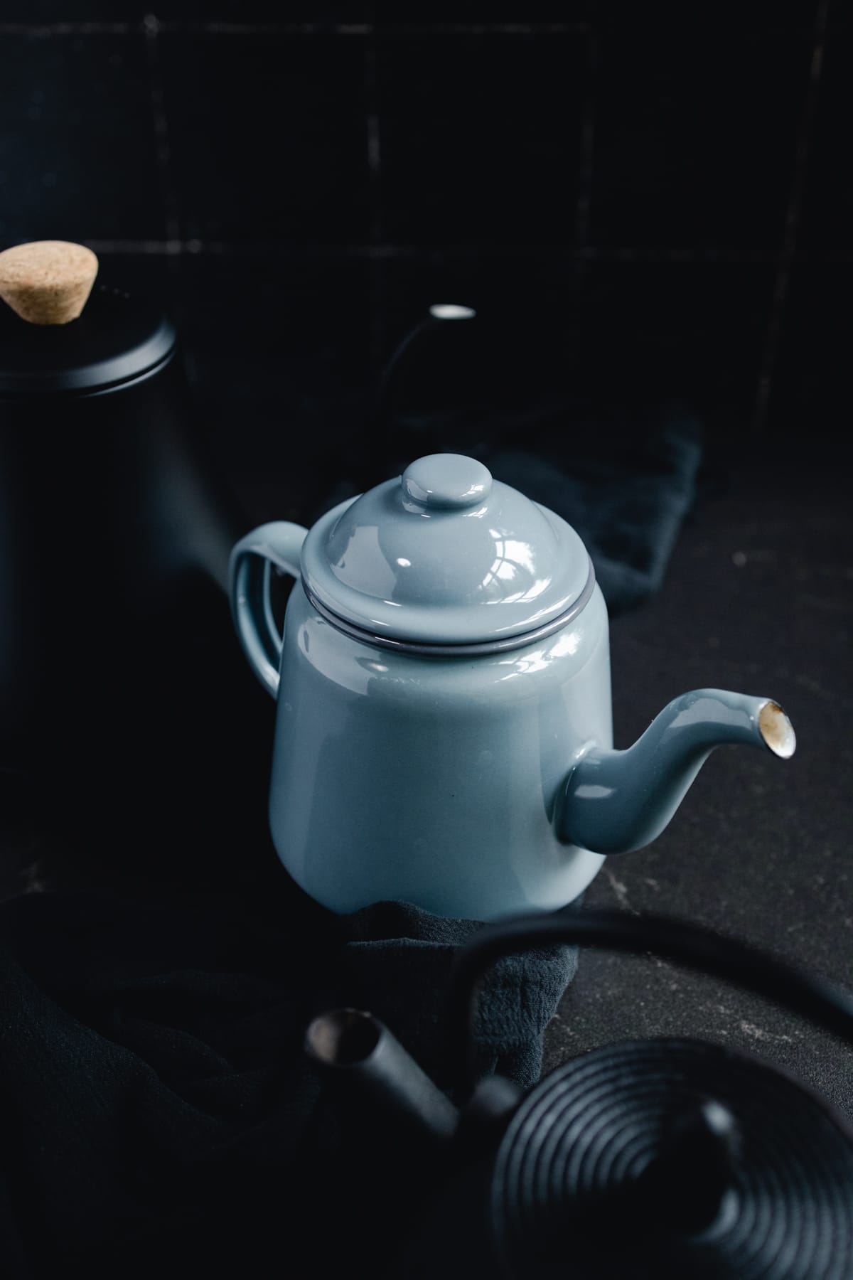 A blue-grey teapot and a black teapot on a table.