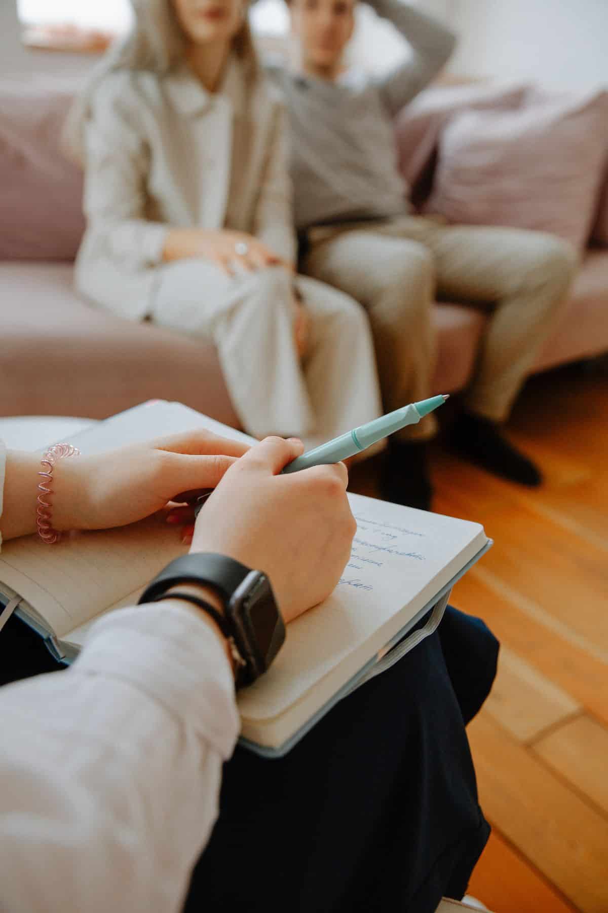 A woman is writing in a notebook while sitting on a couch.