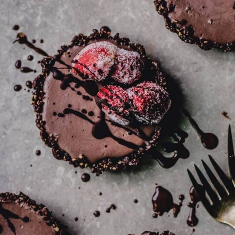 A group of vegan chocolate cheesecakes with strawberries and chocolate drizzle on top.