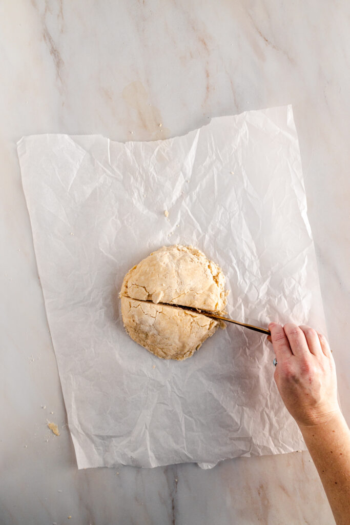 A person cutting a piece of dough on a piece of paper.