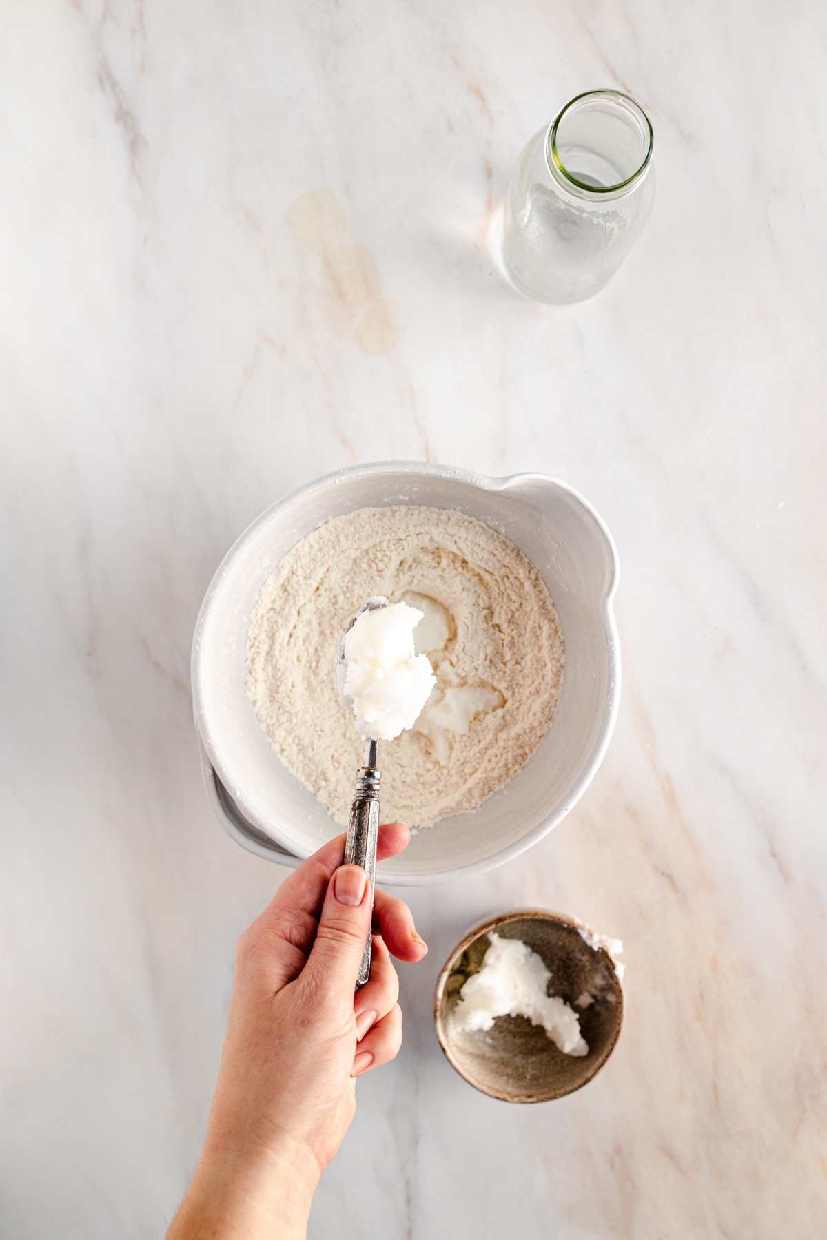 A person pouring a spoonful of flour into a bowl.