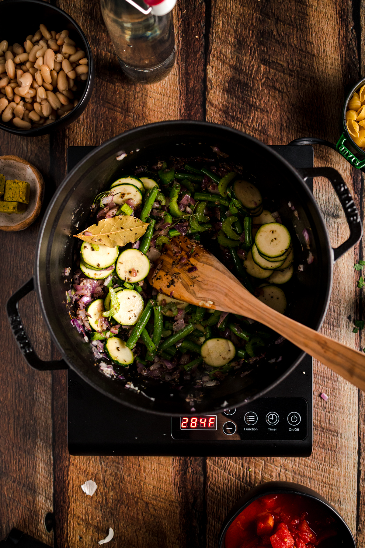 A pot with vegetables and a wooden spoon on a wooden table.