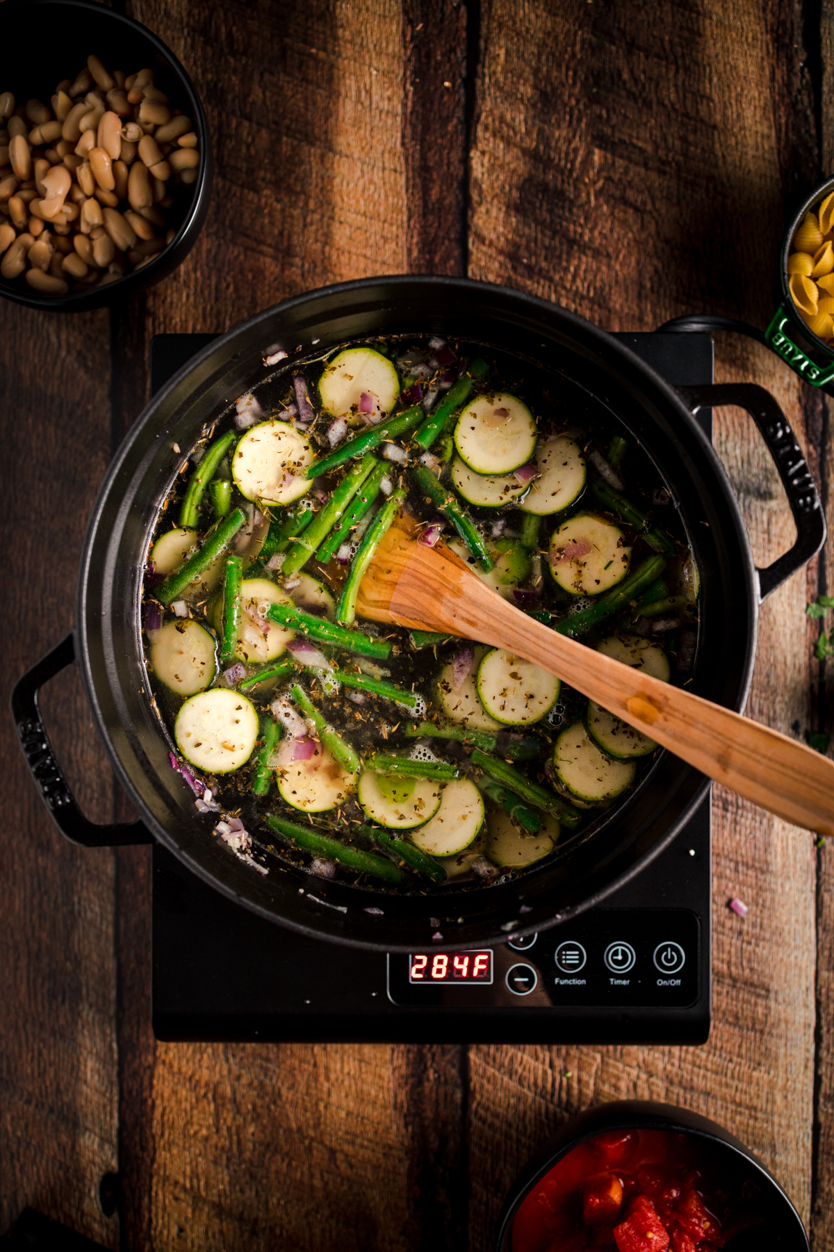 A pot with vegetables and a wooden spoon on a wooden table.