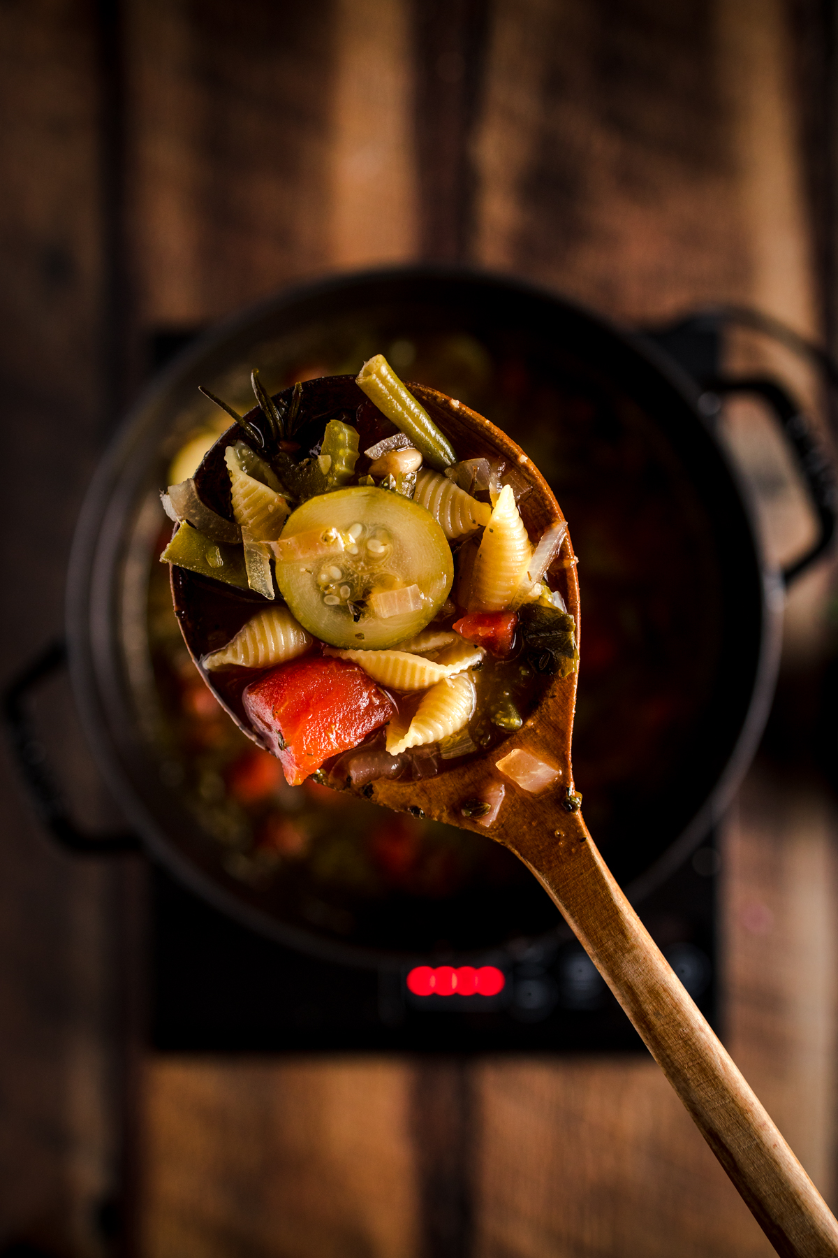 A wooden spoon full of soup on a stove top.