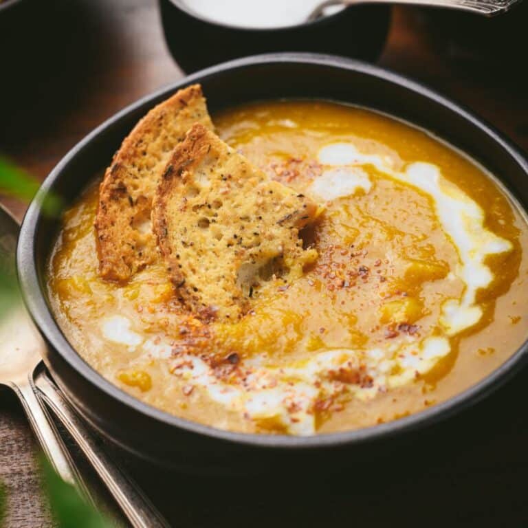 Bowl of creamy pumpkin curry soup topped with two slices of toasted bread and a swirl of coconut milk.