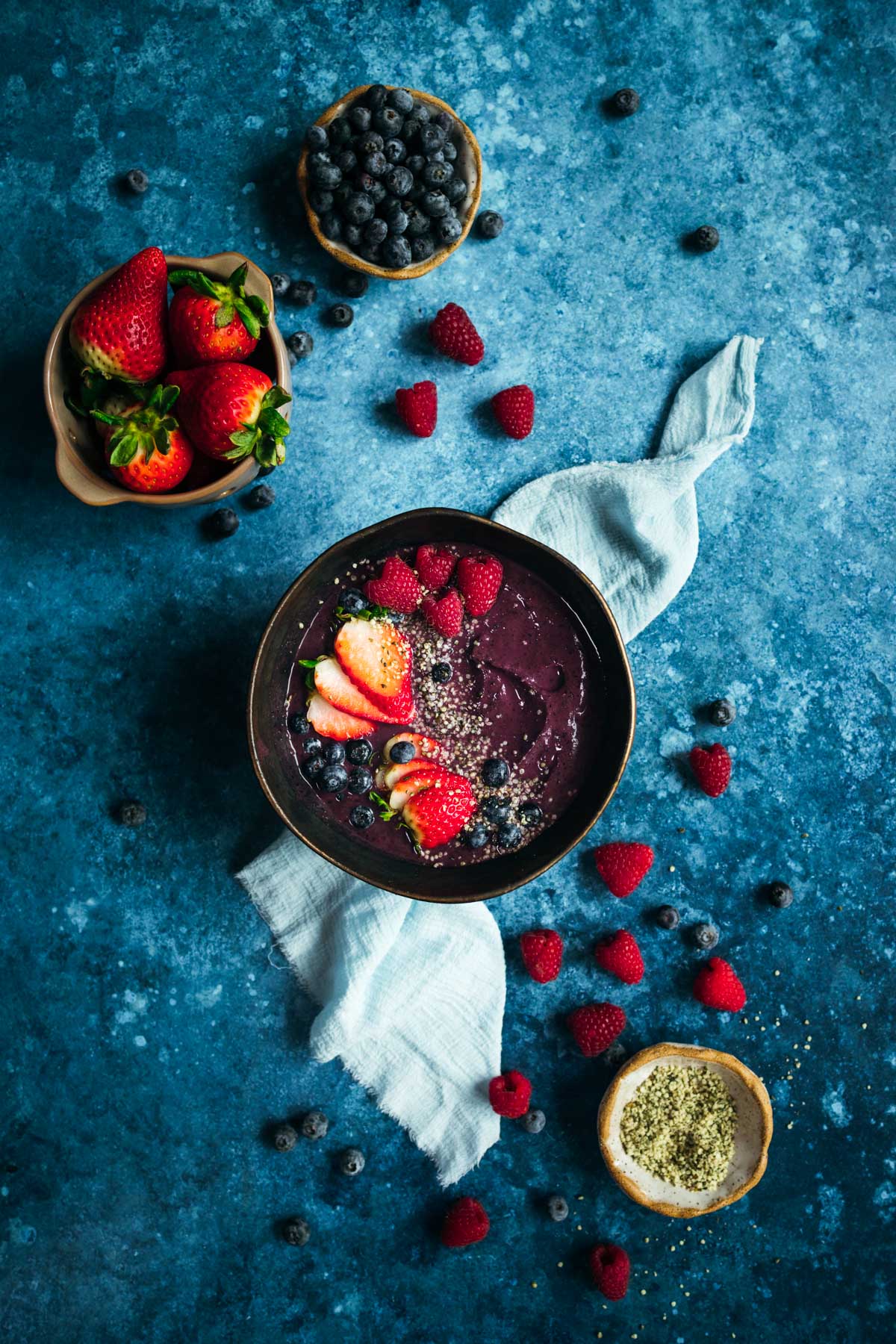 A bowl with berries and hemp seeds and smoothie on a blue background.