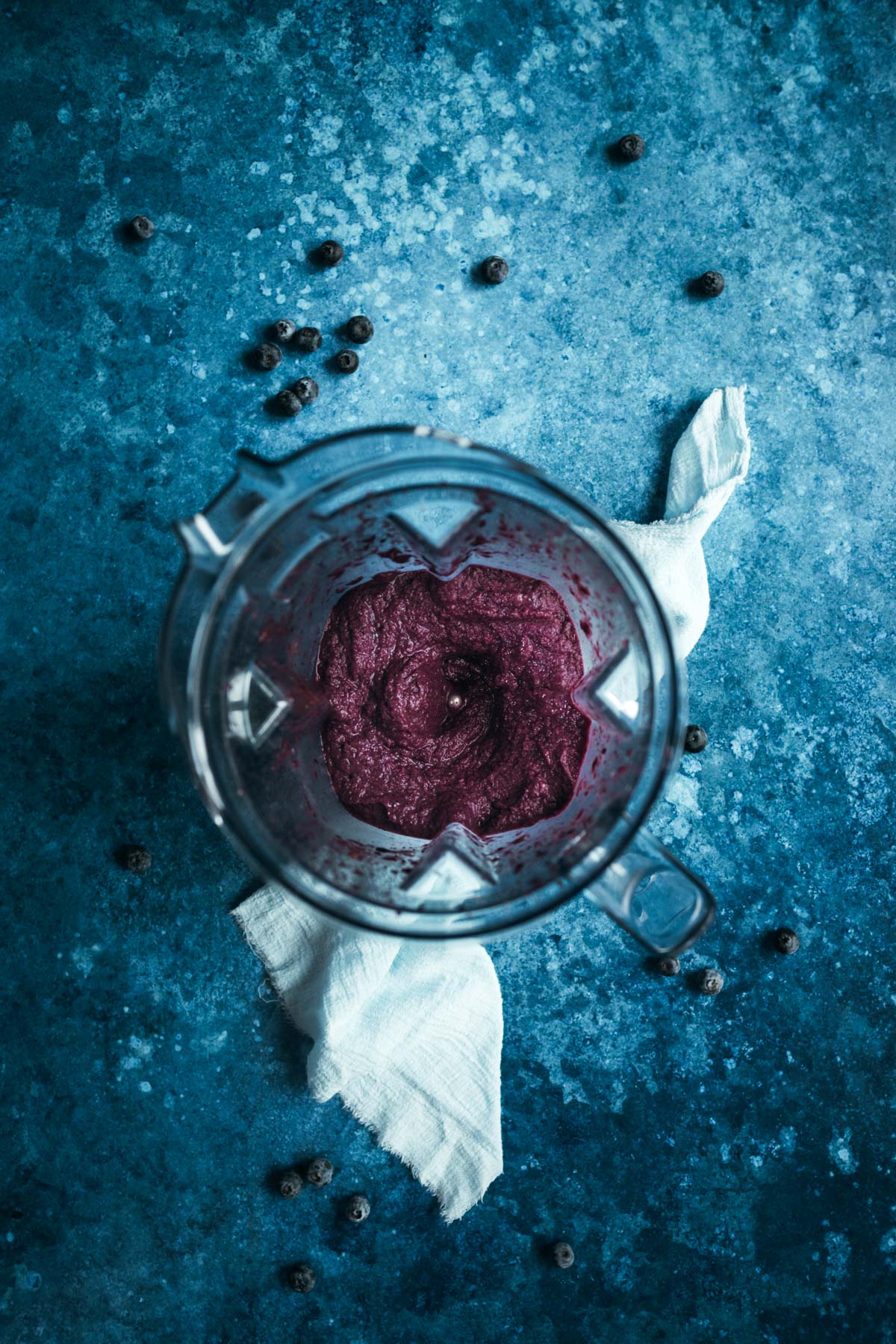 A blender with a mixture of blueberries and a light blue towel.